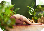 mujer practicando yoga en el interior de una casa rodeada de plantas realizando la postura del niño